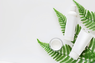 Flat lay with Natural organic cosmetics: cream on white background with green leaves. Skincare, cosmetology, dermatology concept. Top view, mockup, overhead