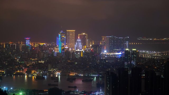 Timelapse bright illuminated Cathedral Parish near flashing Chinese buildings on Macau Peninsula reflected in water with boats at night