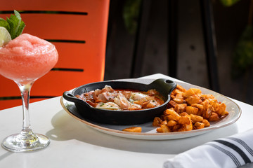 Baked jamon and ham meat with egg skillet with Country Style Fried Potatoes on a pan as a side outside restaurant in a sunny day