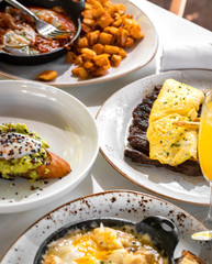 Business lunch of  jamon and ham skillet, toast with avocado and egg, grilled beef with french fries and pan with brussels sprouts with drinks outside a restaurant in a sunny day 