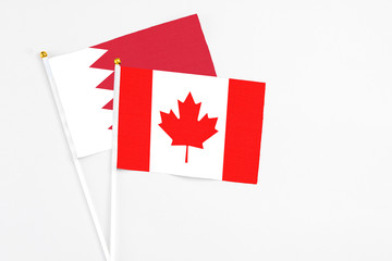 Obraz premium Canada and Bahrain stick flags on white background. High quality fabric, miniature national flag. Peaceful global concept.White floor for copy space.