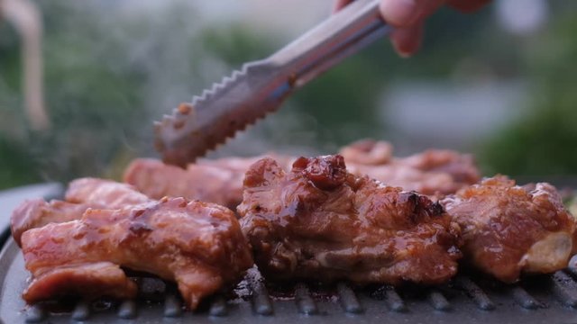 Stock footage HD. Cooked beef steak or pork ribs, toasting meat on a metal electric grill. Royalty high-quality free stock video footage of electric grill stove grilled meat with garden background