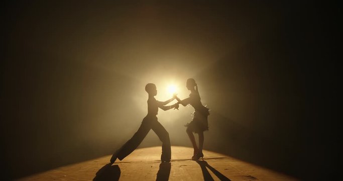 Silhouettes of two little professional ballroom dancers performing a show on stage, spotted by bright light, fullfilling their childhood dream - childhood memories concept 4k footage
