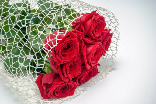 A bouquet with red roses lies on a white table. Presenting picture.