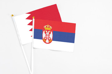 Serbia and Bahrain stick flags on white background. High quality fabric, miniature national flag. Peaceful global concept.White floor for copy space.