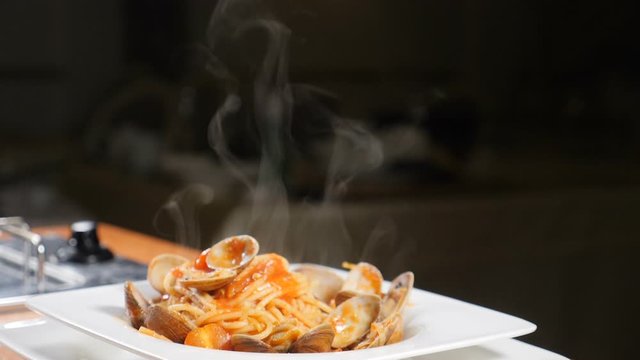 Steaming hot pasta on a square dish. Slow motion. No people. White smoke from spaghetti with sauce - homemade healthy italian pasta on dack background of restaurant. Shot in hd