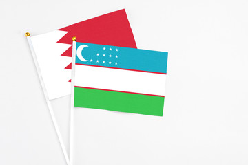 Uzbekistan and Bahrain stick flags on white background. High quality fabric, miniature national flag. Peaceful global concept.White floor for copy space.