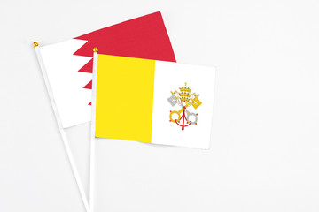 Vatican City and Bahrain stick flags on white background. High quality fabric, miniature national flag. Peaceful global concept.White floor for copy space.