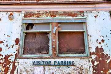 Urban grunge scene of a windows and a peeling wall with a visitors parking sign attached.