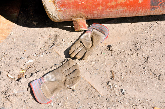 Abandoned construction gloves beside an old rusty metal container.