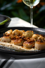 Haute cuisine - grilled king shrimps with white sauce on black dish in outdoors restaurant with glass of white wine