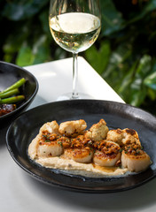 Haute cuisine - grilled king shrimps with white sauce on black dish in outdoors restaurant with glass of white wine