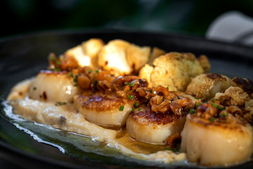 Haute cuisine - grilled king shrimps with white sauce on black dish in outdoors restaurant
