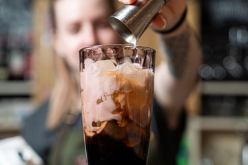 Bartender is making milky alcoholic cocktail pouring and stirring cream into the glass
