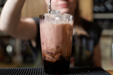 Bartender is making milky alcoholic cocktail pouring and stirring cream into the glass