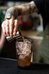 Bartender is making a tropical cocktail on bar counter pouring alcohol and decorating it