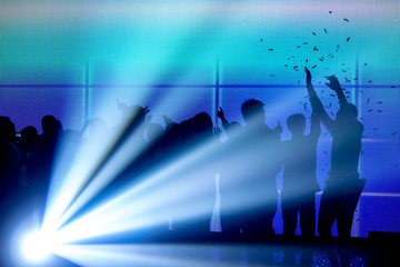 Silhouettes of people celebrate under laser beam and over blue led screen background