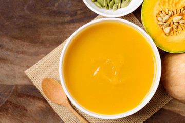 Butternut squash soup in bowl with spoon on wooden background, top view