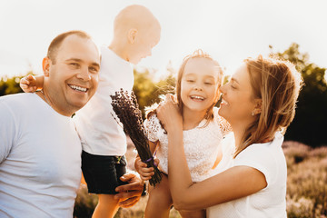 Portrait of a big lovely family playing outdoor in a field of bio flowers laughing against sunset.