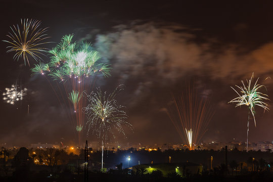 Above the church and the whole city there is a big colorful fireworks in summer. A view over the nocturnal spanish city Elche with rockets and smoke in the air.