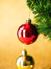 Red christmas ball hanging on pine tree with gold glitter background.