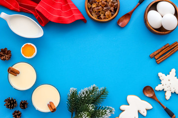Ingredients for New Year drink eggnog - eggs, milk, cinnamon on blue background top view frame copy space