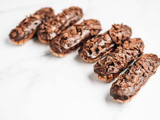 Set of homemade eclairs with chocolate on marble background. Close up view of delicious healthy profitroles with chocolate glaze. Copy space for text or design