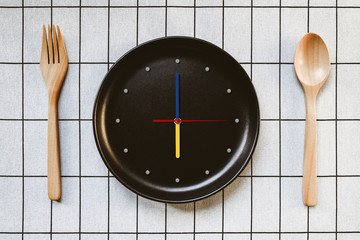 "Time to eat",  Top view of wooden spoon and fork with black clock plate, white pattern table background, with blank copy space