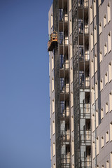 An external open building elevator rises with workers along the