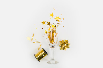 Glass of champagne with glitter and holiday decorations and gift box on a white background, top view. New Year or Christmas