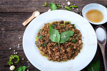 Stir-fried minced pork with basil in a white ceramic dish and put ingredients on a wooden table. Close up shot. 45 degree angle.