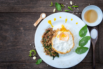 Basil fried pork with fried egg in a white ceramic dish placed on a wooden table. Close up shot. Top view.