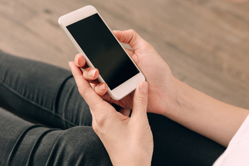 Woman hand holding white mobile phone and sitting on sofa at home.