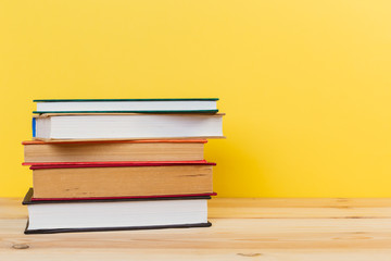 Simple composition of many hardback books, raw of books on wooden table and pastel yellow background