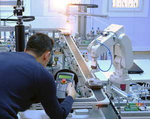Industry 4.0 concept: An engineer is programming robotic arm with control panel (teach pendant)...