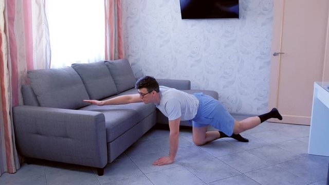Funny nerd man in glasses and shorts is doing balance pose on all fours at home. Sport humor concept.