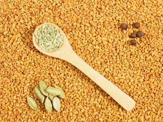 Spices in spoon – fennel, green cardamom, allspice. Background from Fenugreek. Indian cuisine ingredients