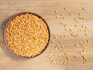 Fenugreek in clay plate on a brown wooden background. Indian cuisine, ayurveda, naturopathy, modern apothecary concept