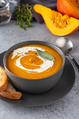 Pumpkin soup with cream on grey stone background. Copy space.