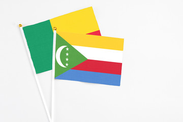 Comoros and Benin stick flags on white background. High quality fabric, miniature national flag. Peaceful global concept.White floor for copy space.