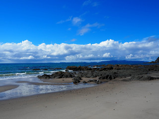 black volcanic rocks on a sandy beach against the background of the ocean and bright blue sky