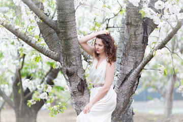 A portrait of beautiful young Caucasian woman with curly dark hair in blossoming orchard