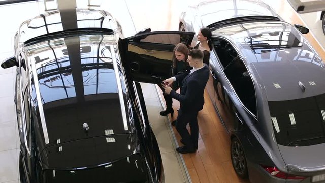 Two gorgeous girls talking to a sales consultant in a car dealership, they want to buy a new car. The process of working in the showroom.