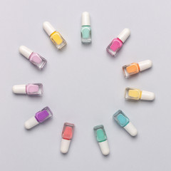 Nail polish bottles laid out in a circle shape grey background. Top view, copy space.