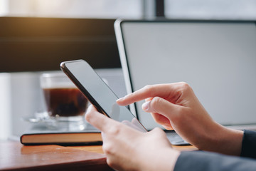 Woman holding smartphone with blank white screen and laptop on wooden table can be add your texts or others, empty copy space for advertising, product display.