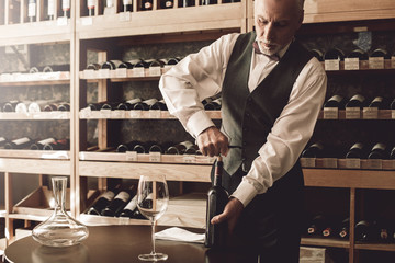 Sommelier Concept. Senior man standing opening wine bottle with corkscrew concentrated