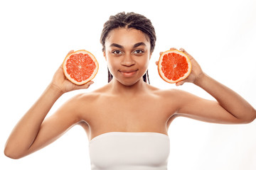 Beauty Concept. Young african woman wearing top isolated on white with grapefruit halves smiling confident
