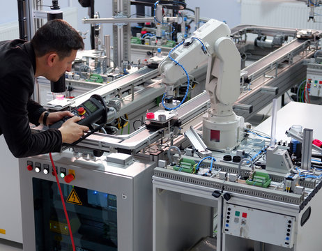 industry 4.0 concept: Man (engineer) is programming robotic arm with control panel (teach pendant) on smart factory production line background. Selective Focus.