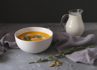 Pumpkin Soup with Rosemary, seeds and cream on gray concrete background