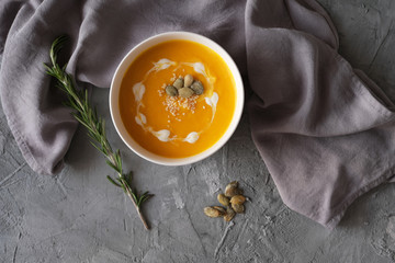 Pumpkin soup with rosemary, seeds and cream on gray concrete background